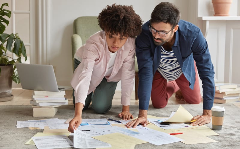 Two people sitting on the floor sorting financial documents Two people sitting on the floor sorting financial documents